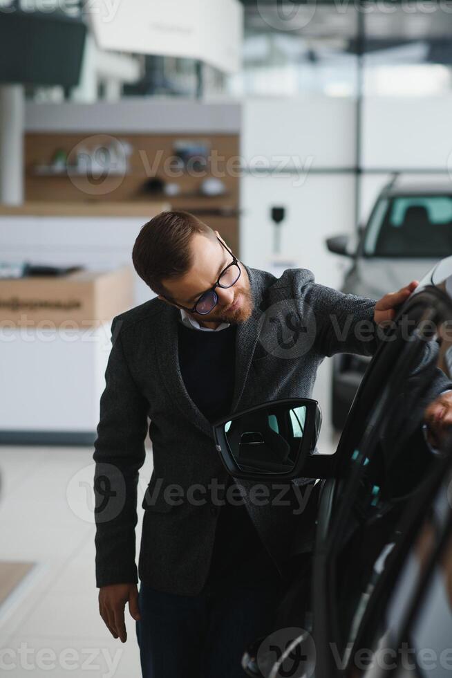 Man adult customer male buyer client wears classic suit white shirt chooses auto wants to buy new automobile touch check car in showroom vehicle salon dealership store motor show indoor photo