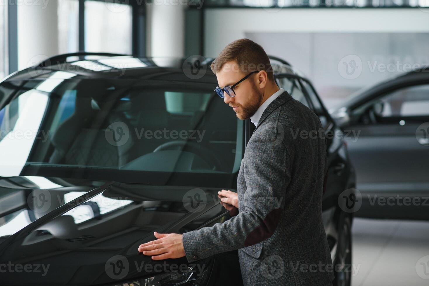 Visiting car dealership. Handsome bearded man is stroking his new car and smiling photo