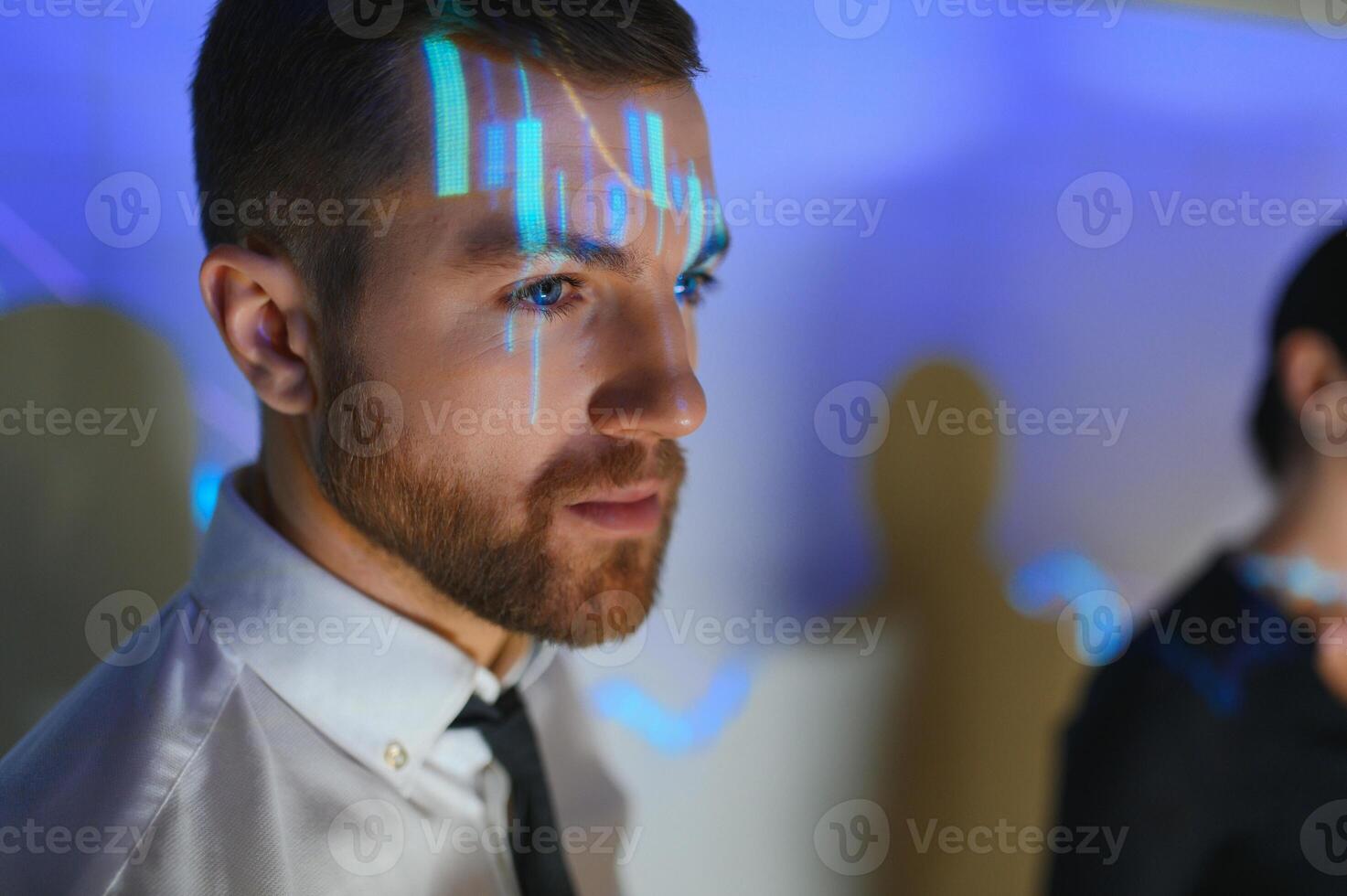 Stock Market Top Trader Looks at Projected Ticker Numbers and Graphs Running, Analysing Data to Make Best Sell. Behind Him Room Full of Screens and Statistics. photo