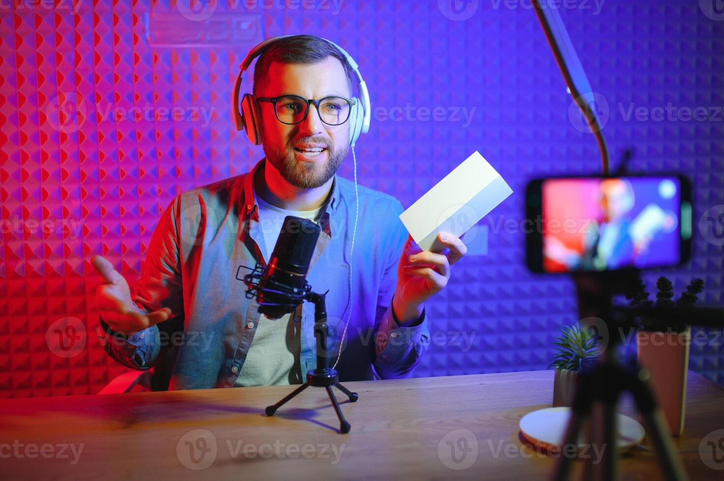 Male technology blogger recording blog or vlog review of new smartphone, showing it on camera at home studio. Blogging, Work from Home concept. Selective focus. Web Banner photo