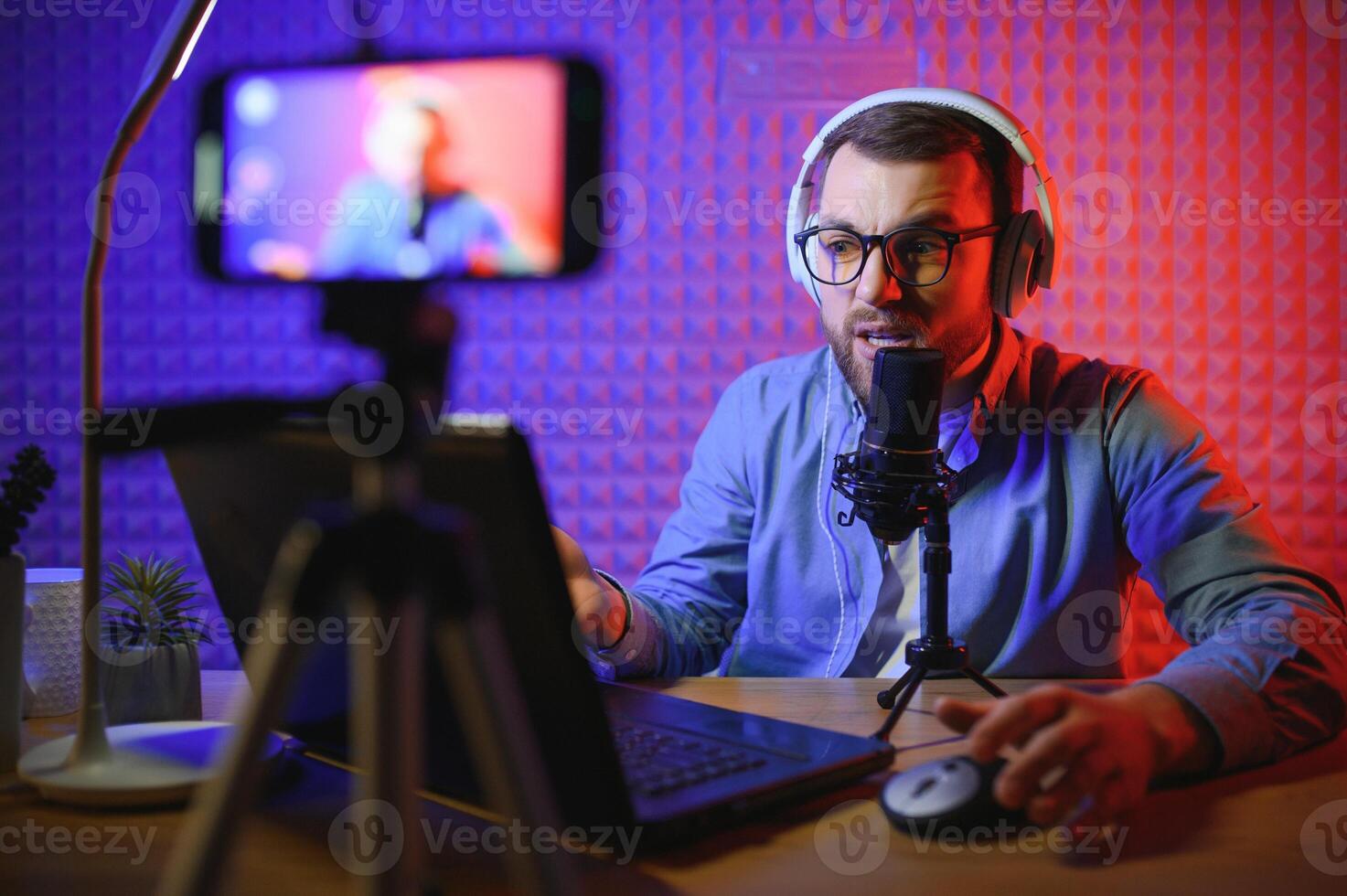 Young man recording or streaming podcast using microphone at his small broadcast studio. Content creator. photo