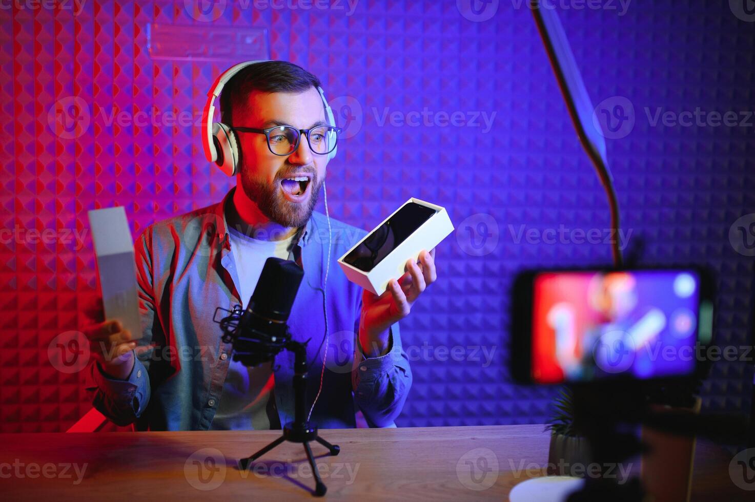 Male technology blogger recording blog or vlog review of new smartphone, showing it on camera at home studio. Blogging, Work from Home concept. Selective focus. Web Banner photo
