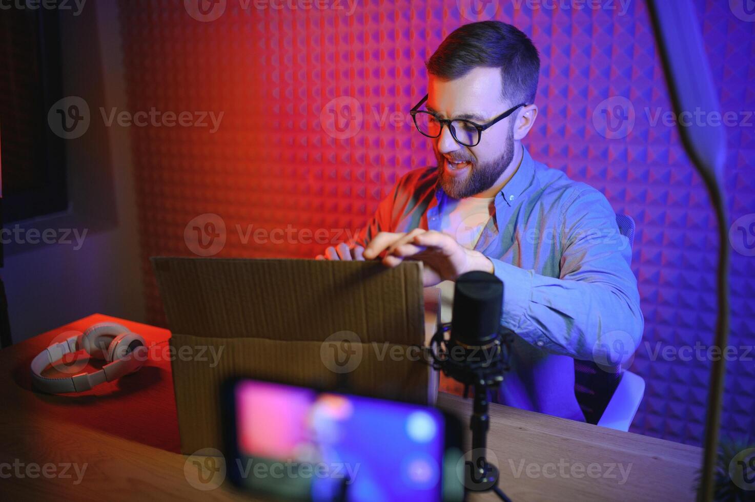Handsome young man gesturing while unpacking parcel, excited, clenches fists in triumph. Joyful male vlogger. Concept of people and social networks. photo