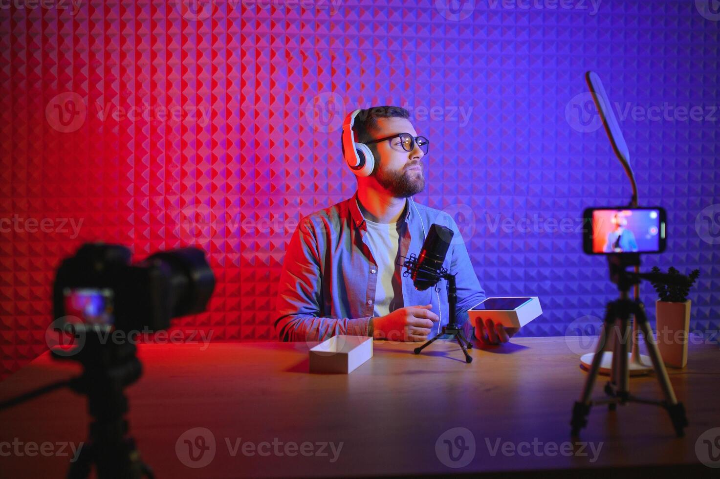 Male technology blogger recording blog or vlog review of new smartphone, showing it on camera at home studio. Blogging, Work from Home concept. Selective focus. Web Banner photo