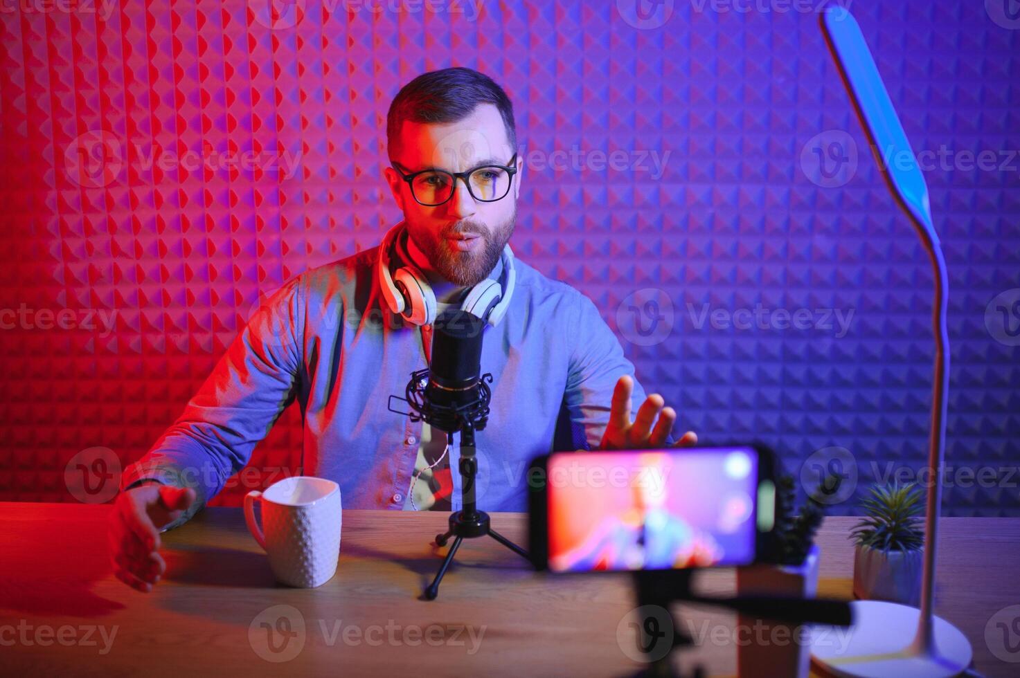 Young man recording or streaming podcast using microphone at his small broadcast studio. Content creator. photo