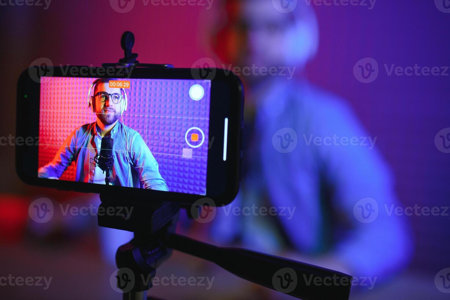 vlogger using smartphone to film podcast in studio. blogger with mobile phone, microphone and headphones filming for social media broadcasting career. photo