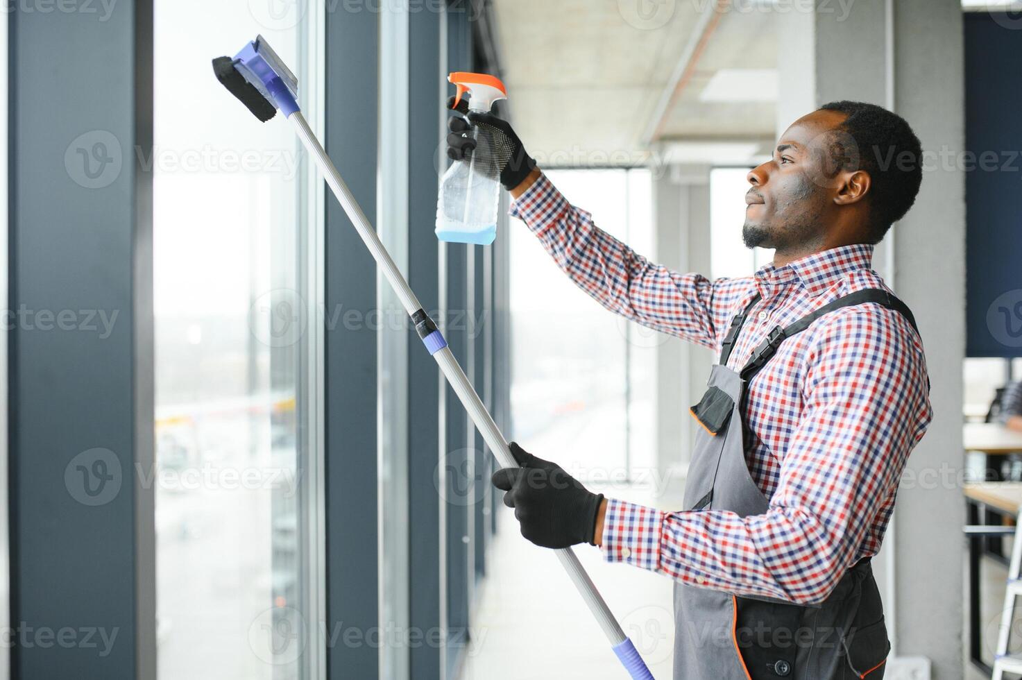 worker of cleaning organization carefully and carefully rubs large window of the office space. A serious African-American in blue overalls wipes the double-glazed window in the office photo