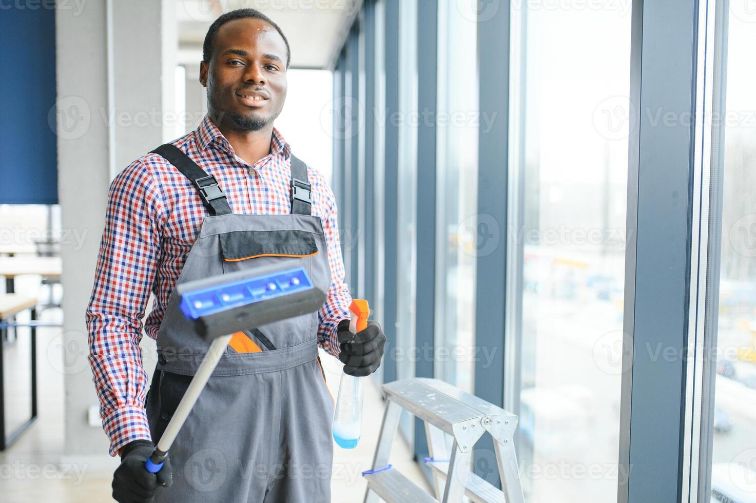 African Male professional cleaning service worker in overalls cleans the windows and shop windows of a store with special equipment photo