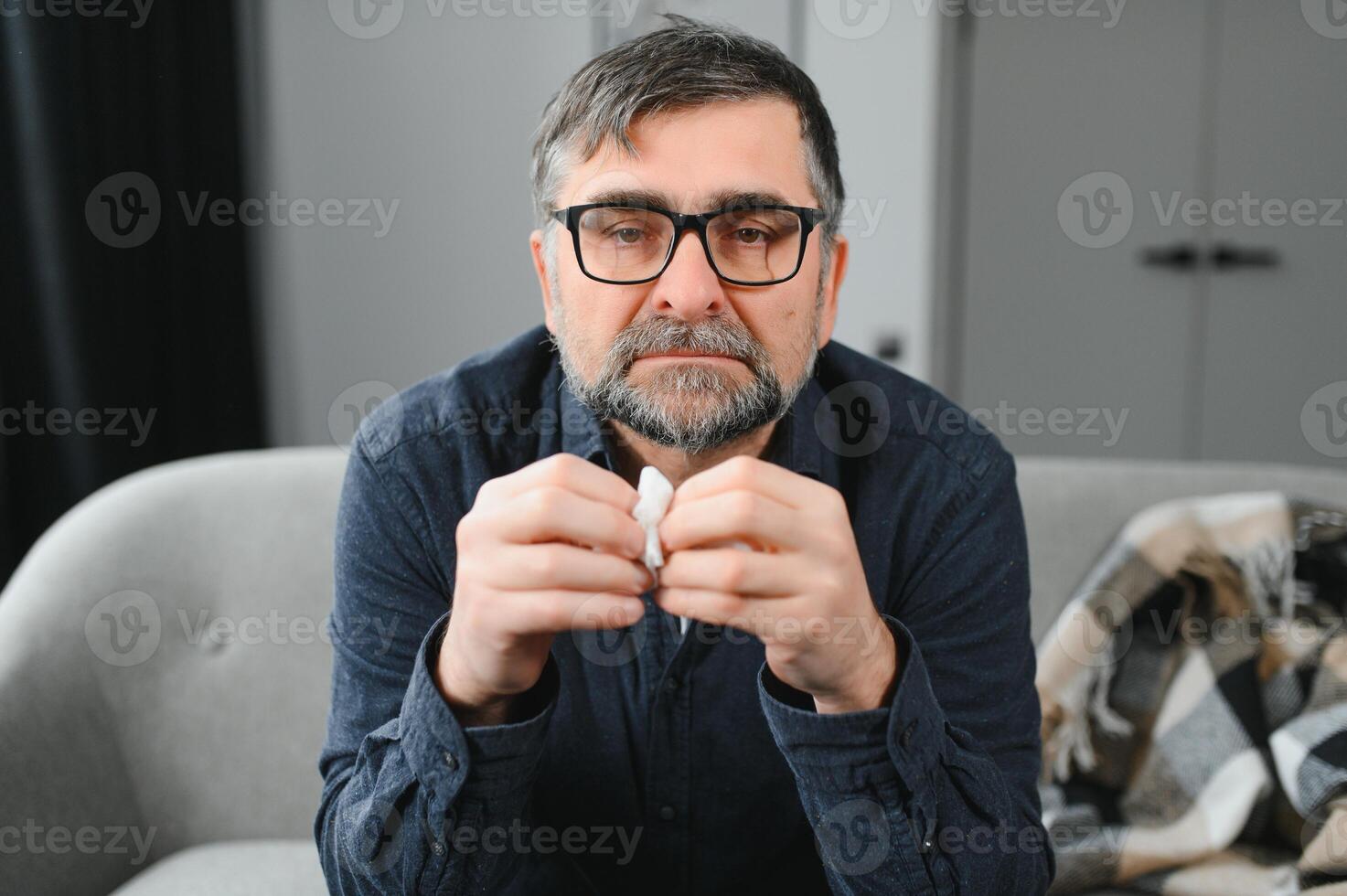 healthcare, flu, hygiene and people concept - sick senior man with paper wipe blowing his nose at home photo