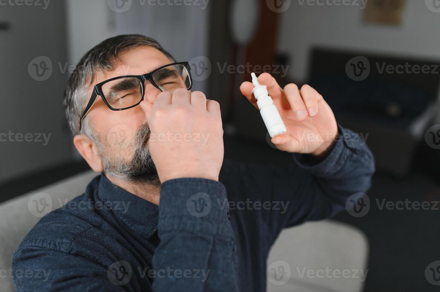 Portrait of man with a nasal spray. Sick man using nose drops while laying at the bed. Concept of treatment for allergies or the common cold, winter style. photo