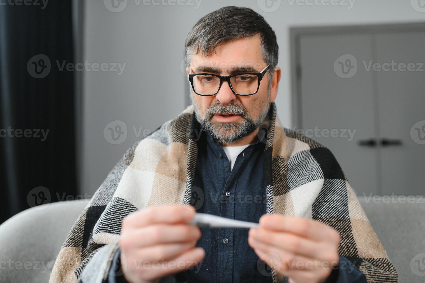 Portrait of sick senior man with thermometer posing at home photo