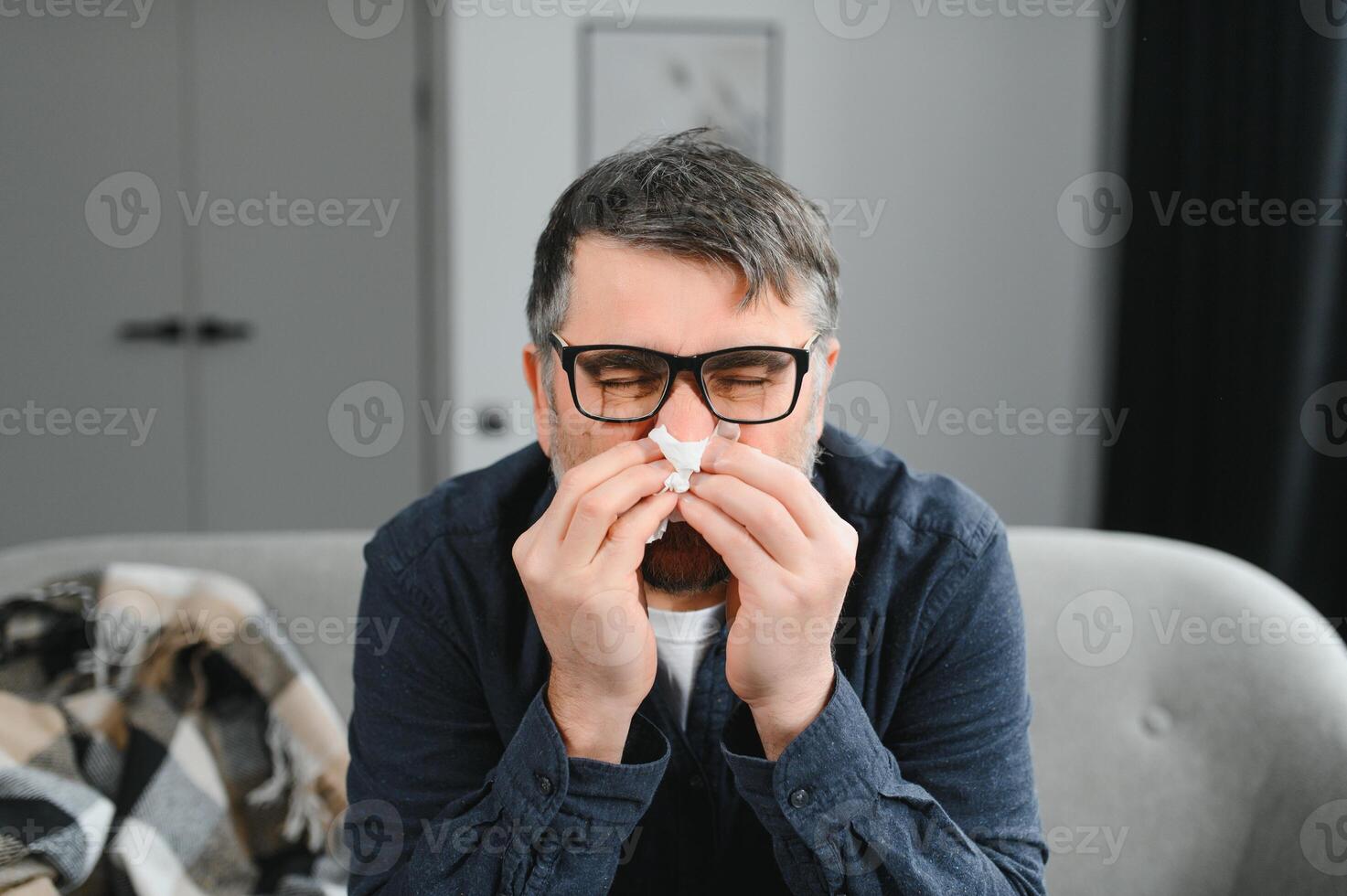 healthcare, flu, hygiene and people concept - sick senior man with paper wipe blowing his nose at home photo