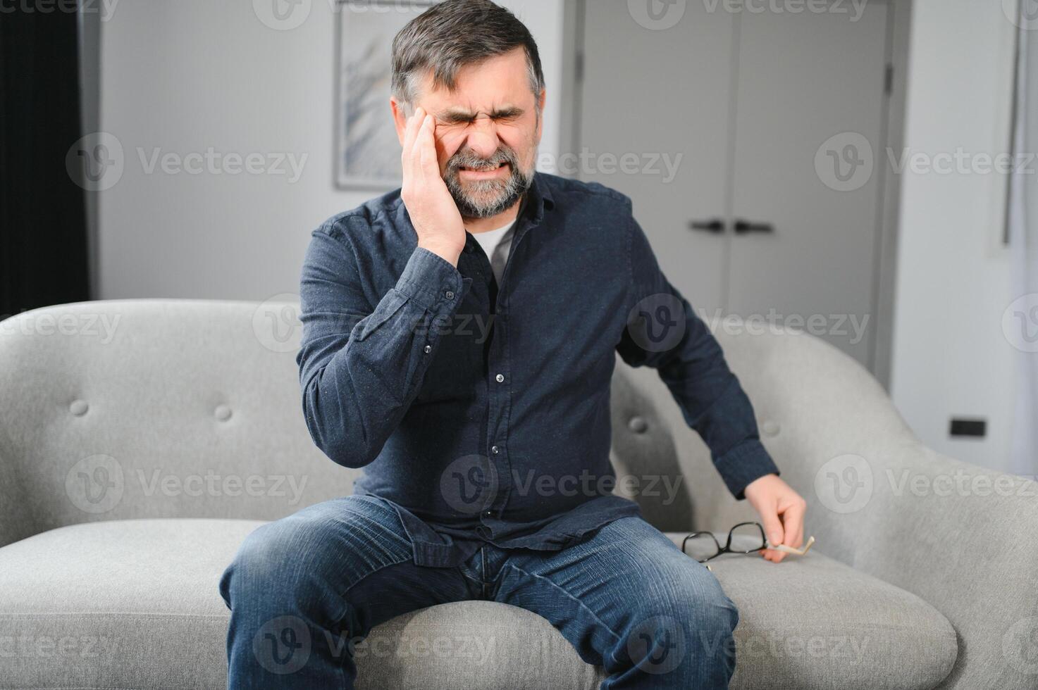 Closeup of middle-aged bearded man suffering from headache at home, touching his temples, panorama with copy space. Migraine, headache, stress, tension problem, hangover concept photo