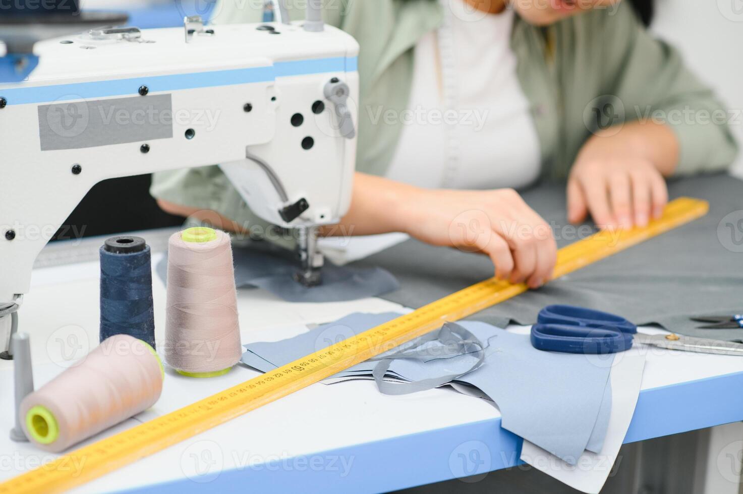 Cheerful young seamstress sits at the table with working things, in atelier photo