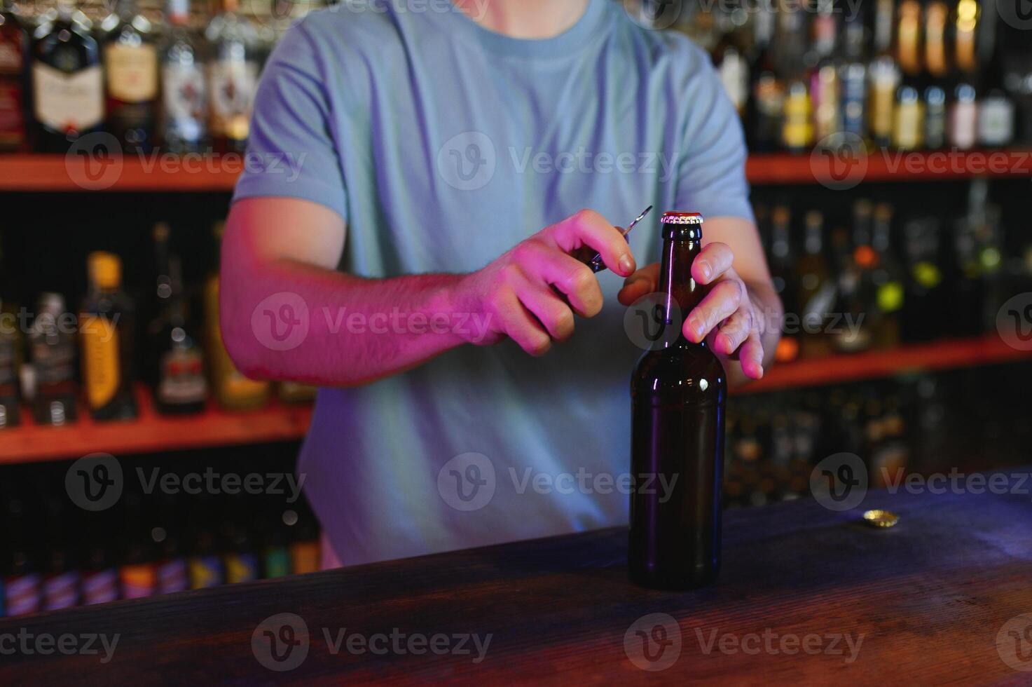 Barman bottle of beer. Nearby empty glass on wooden bar counter in interior of pub, cropped, free space. photo