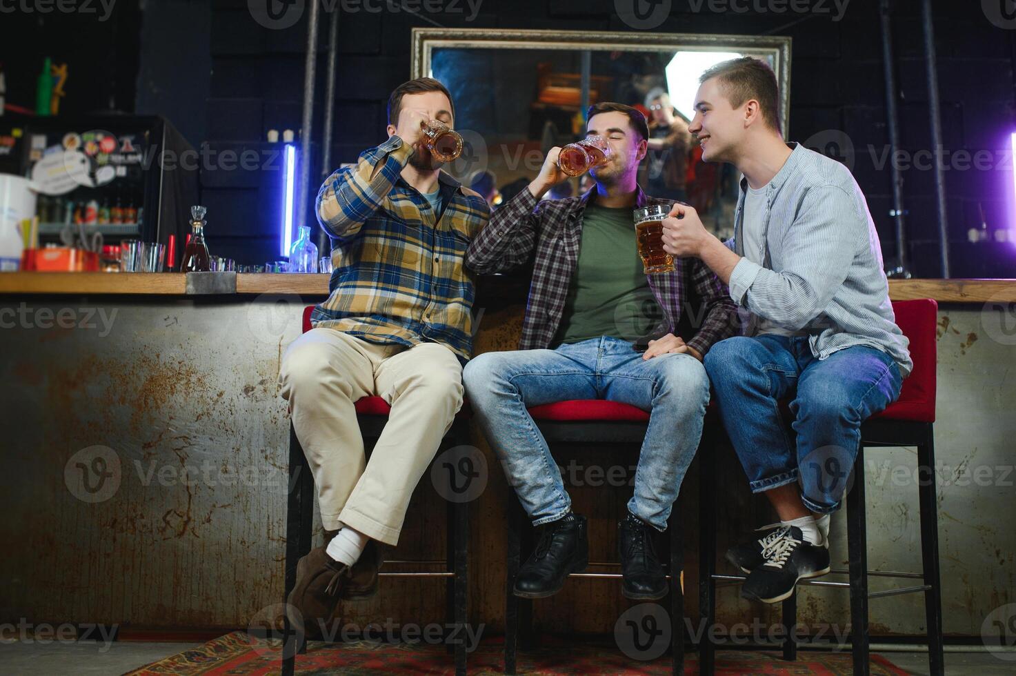Young men in casual clothes are talking, laughing and drinking while sitting at bar counter in pub photo