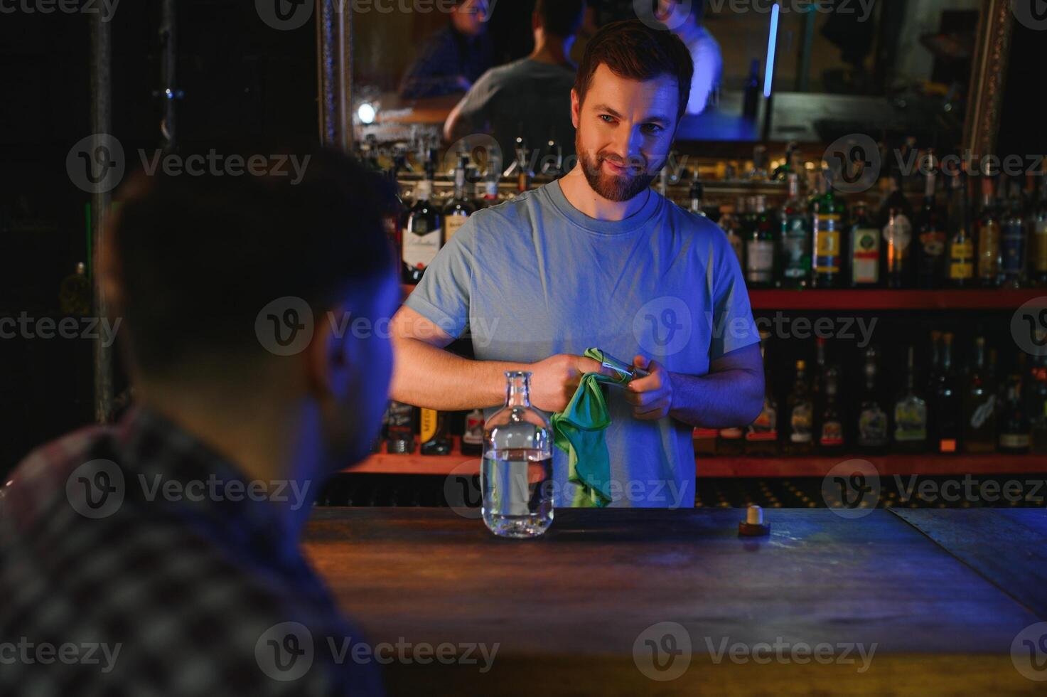 Barman pouring hard spirit into glasses for two male friends relaxing in a bar photo