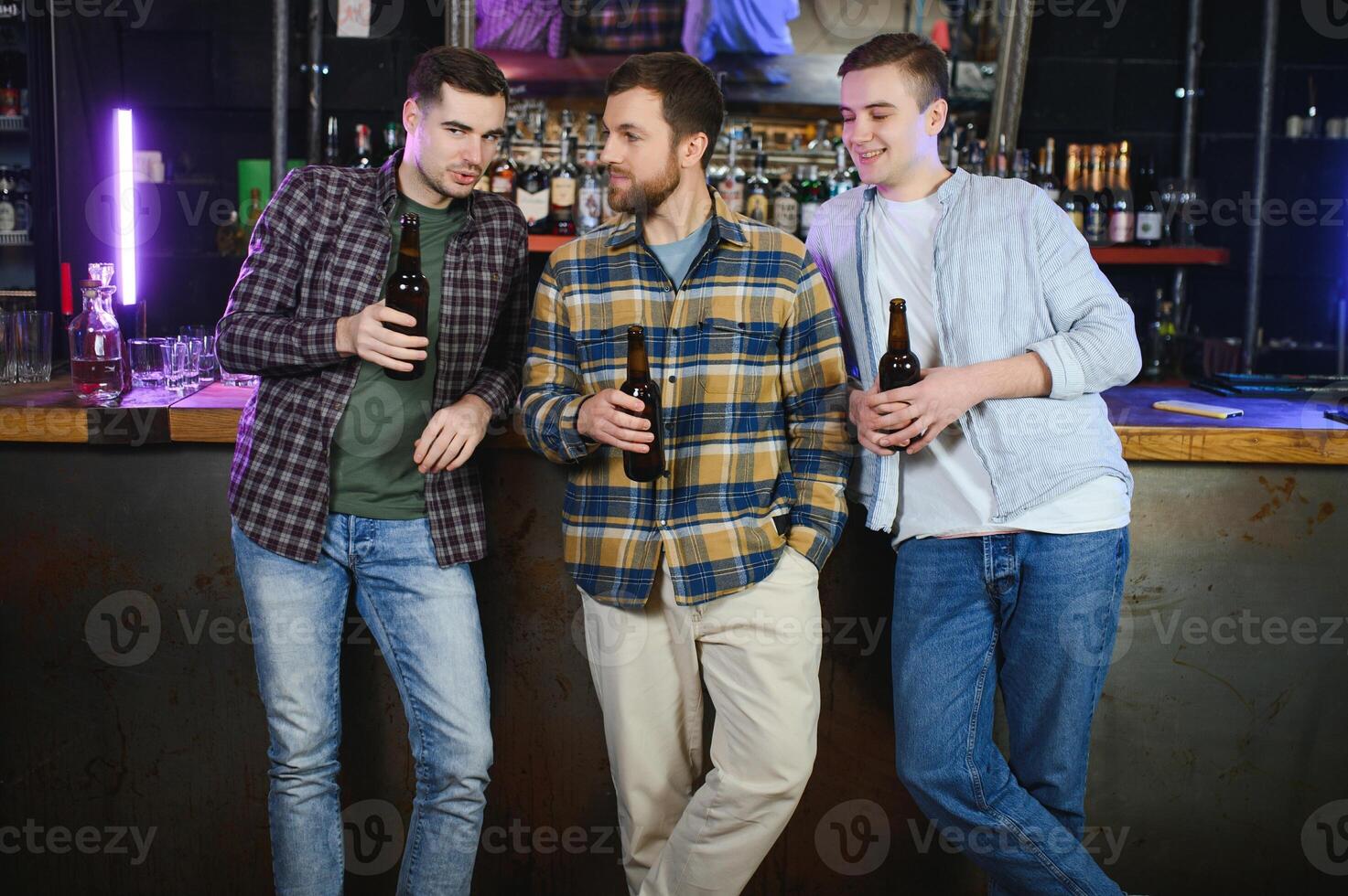 Young men in casual clothes are talking, laughing and drinking while sitting at bar counter in pub photo