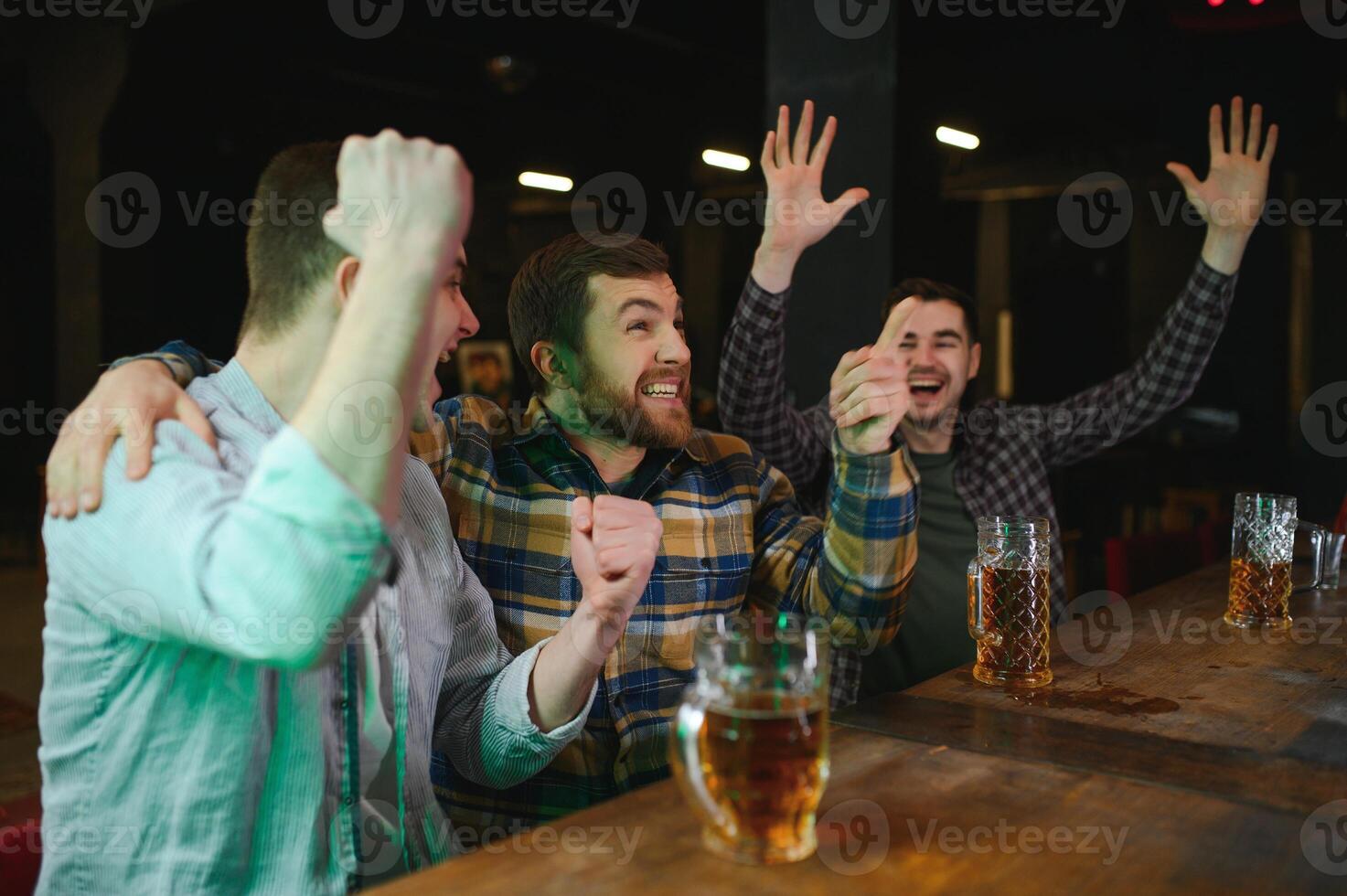 Soccer fans cheering for favourite team while enjoying drinks. Group of supporters celebrating victory while watching football match on tv in a club. Happy friends shouting while cheering for a goal. photo