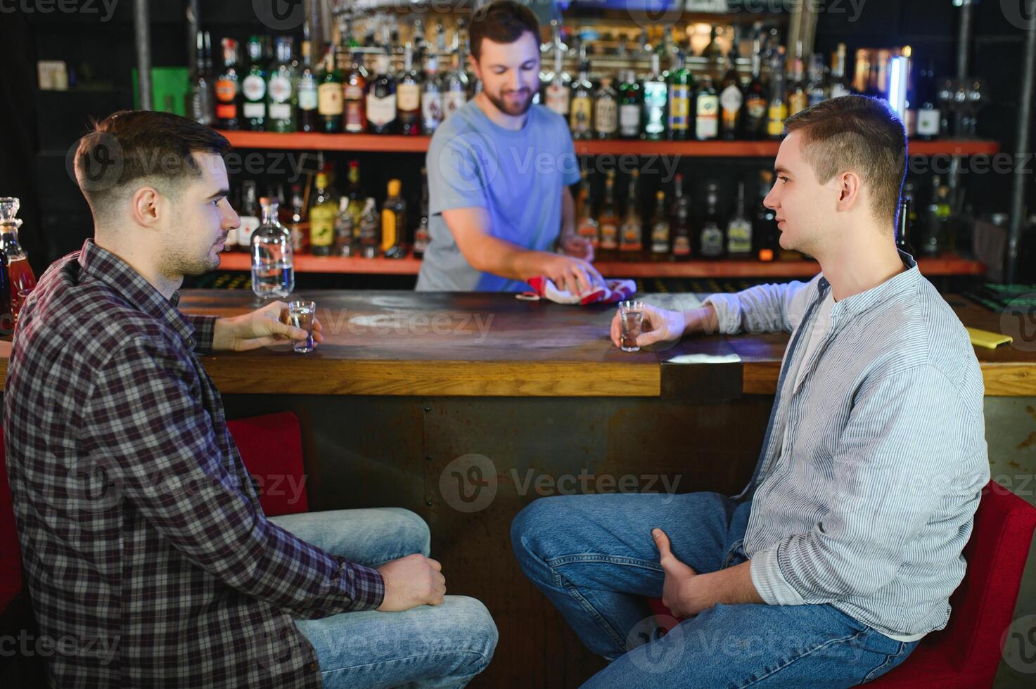 Young men in casual clothes are talking, laughing and drinking while sitting at bar counter in pub photo