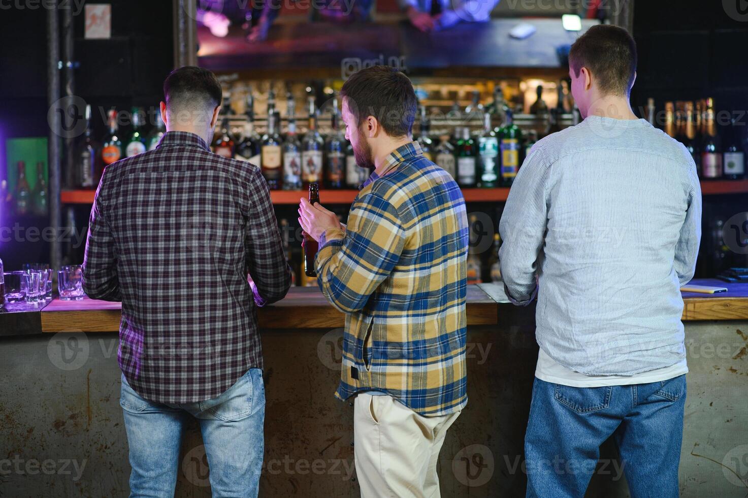 Young men in casual clothes are talking, laughing and drinking while sitting at bar counter in pub photo