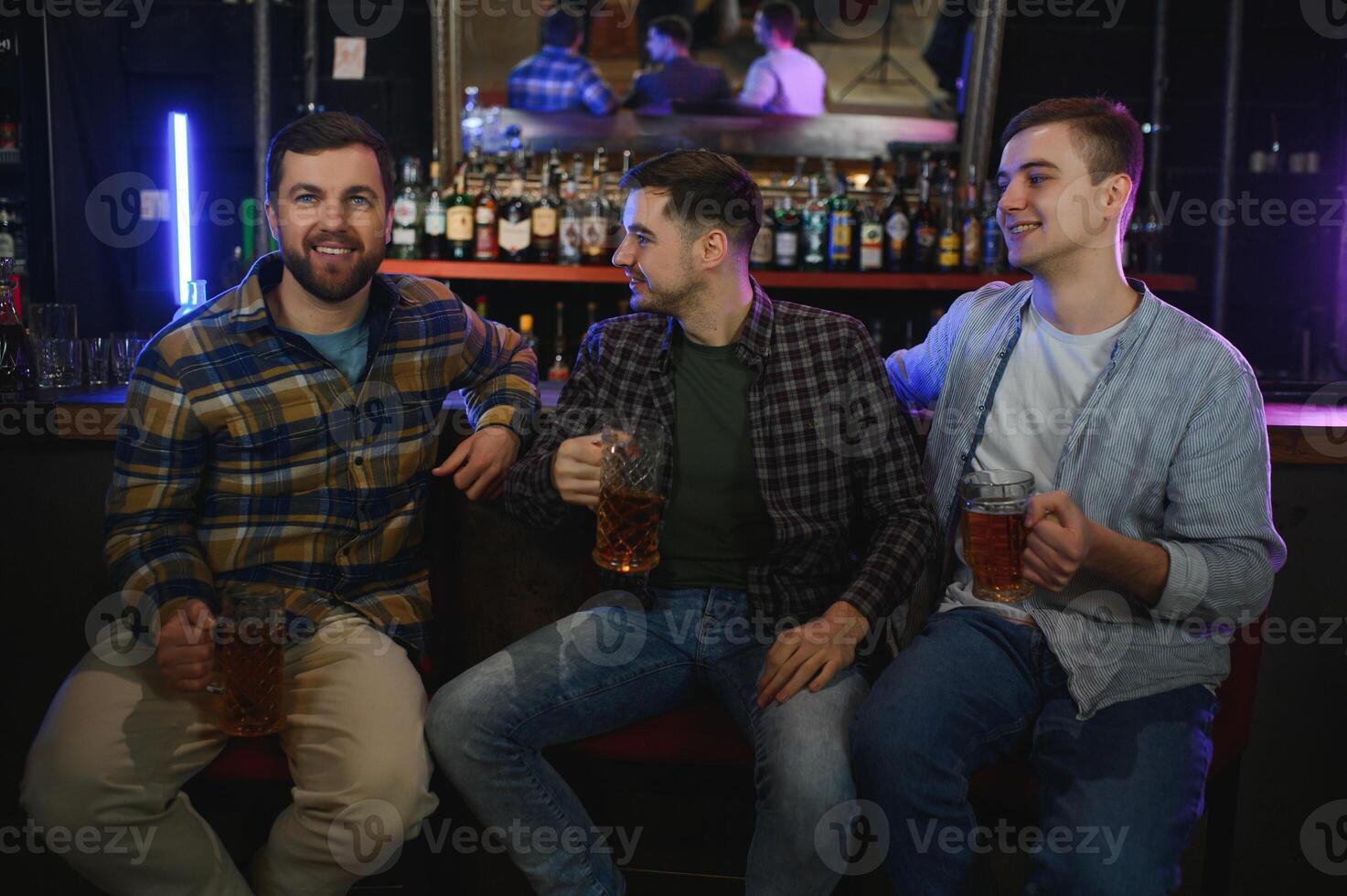 Young men in casual clothes are talking, laughing and drinking while sitting at bar counter in pub photo
