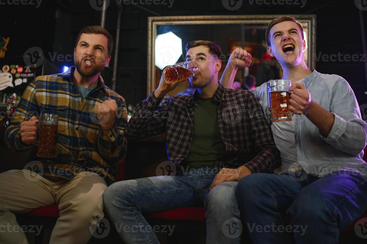 Soccer fans cheering for favourite team while enjoying drinks. Group of supporters celebrating victory while watching football match on tv in a club. Happy friends shouting while cheering for a goal. photo