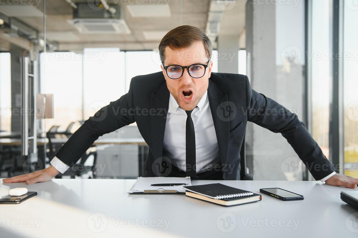 Angry businessman sitting at his desk and screaming at his employees. photo