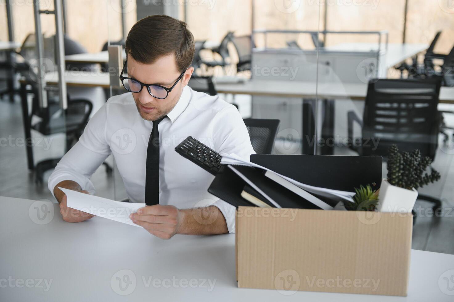 Young handsome businessman in light modern office with carton box. Last day at work. Upset office worker is fired. photo