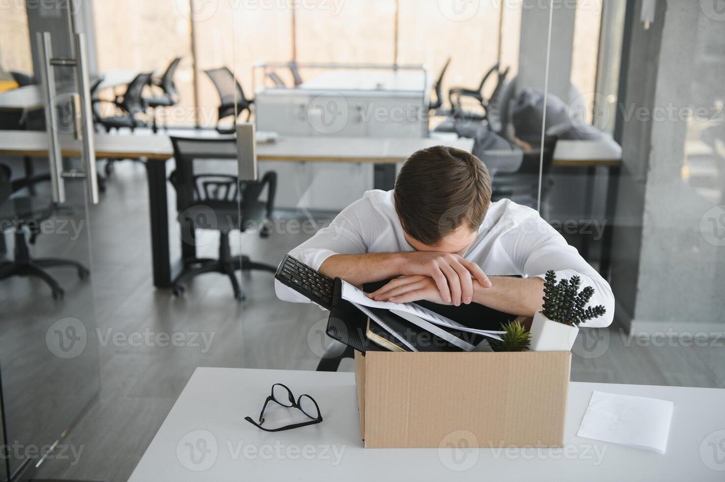 Sad Fired. Let Go Office Worker Packs His Belongings into Cardboard Box and Leaves Office. Workforce Reduction, Downsizing, Reorganization, Restructuring, Outsourcing. Mass Unemployment Market Crisis photo