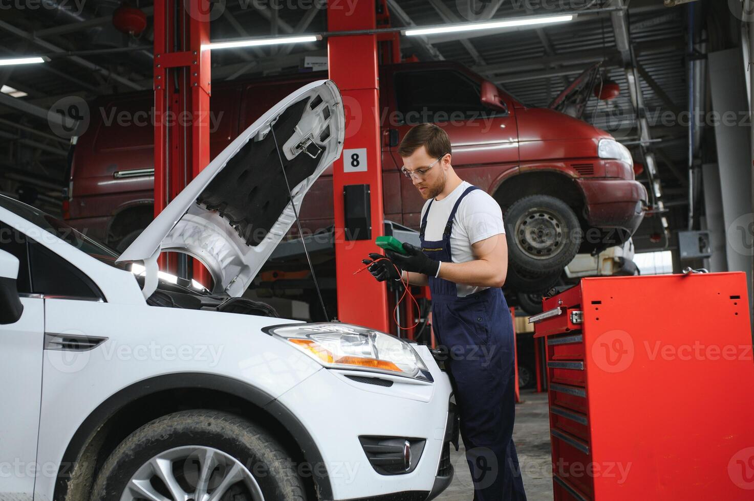 With tool in hand. Adult man in colored uniform works in the automobile salon photo