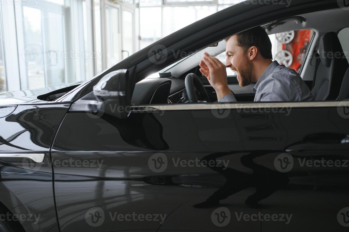 Happy young driver behind the wheel inside new car. Lifestyle scene in the car dealership photo