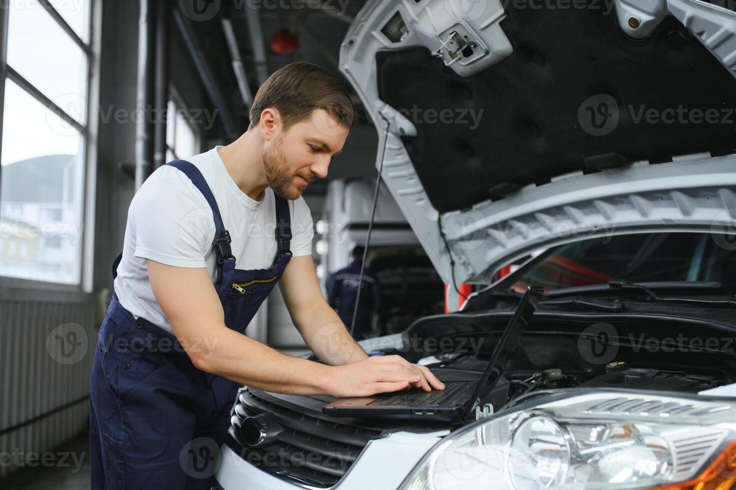 With laptop. Adult man in uniform works in the automobile salon. photo