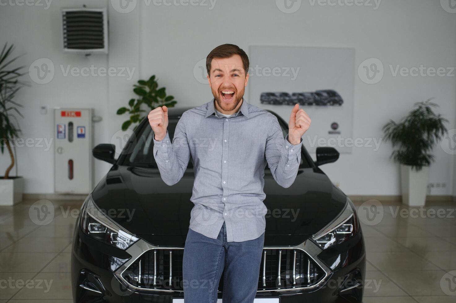 Emotional handsome guy raising hand up and smiling at camera. Rich man buying auto at luxury dealership salon photo