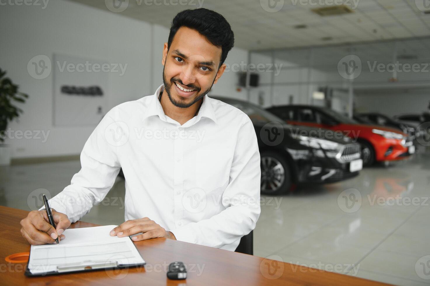 young indian man signing documents at car dealership photo