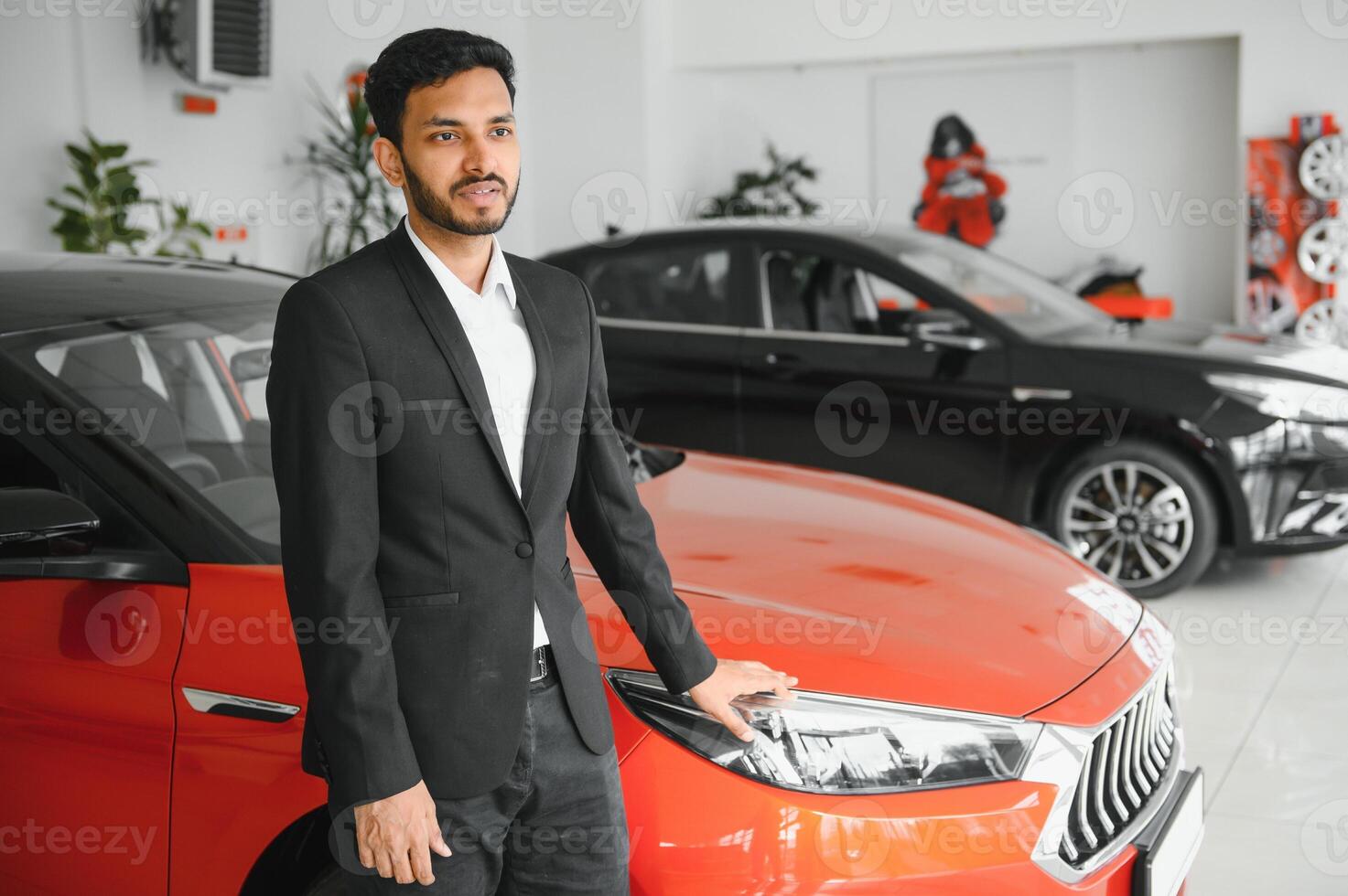 Smiling, friendly indian car seller standing in car salon. photo