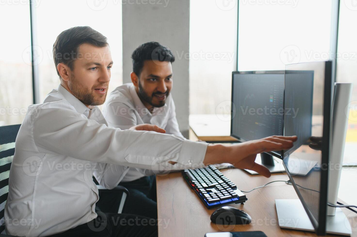 Two successful trader sitting in office and looking at screen, checking cryptocurrency information data on finance market graph, pointing on monitor photo