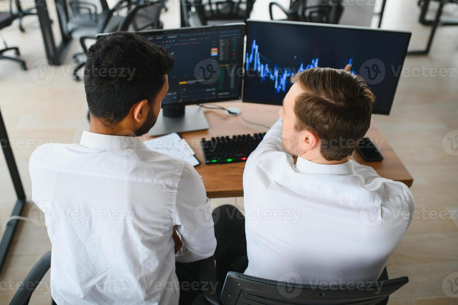 Two successful trader sitting in office and looking at screen, checking cryptocurrency information data on finance market graph, pointing on monitor photo