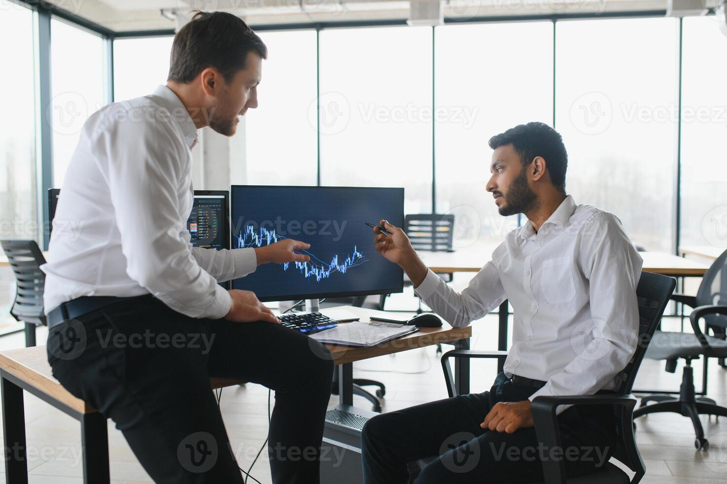 Two men traders sitting at desk at office together monitoring stocks data candle charts on screen analyzing price flow smiling cheerful having profit teamwork concept photo