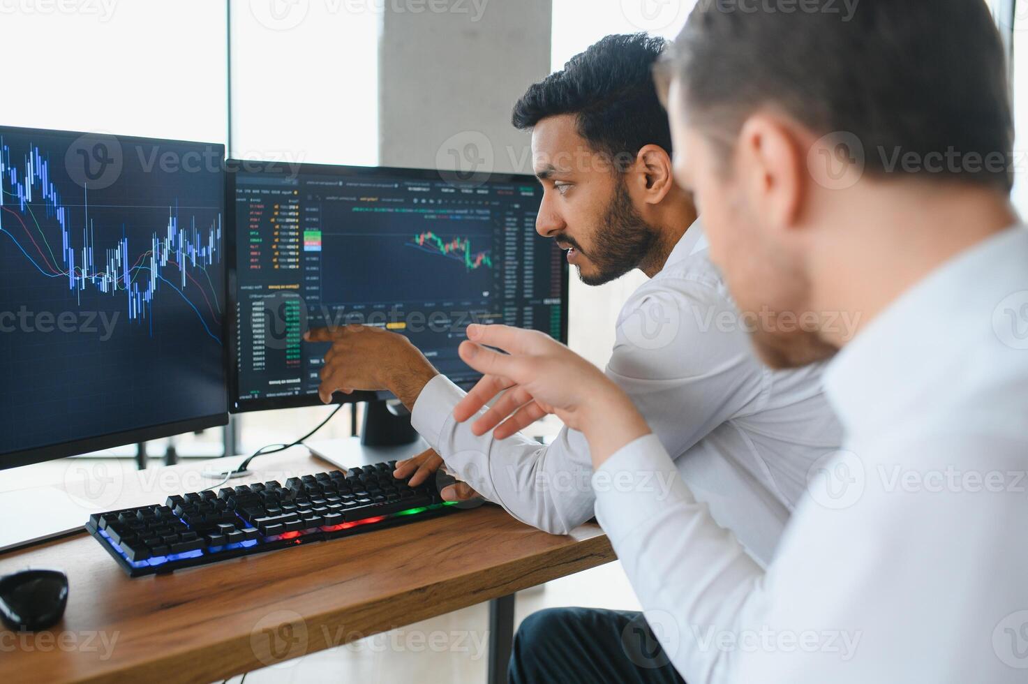 Two men traders sitting at desk at office together looking at data analysis discussing brainstorming successful strategy inspired teamwork concept close-up photo