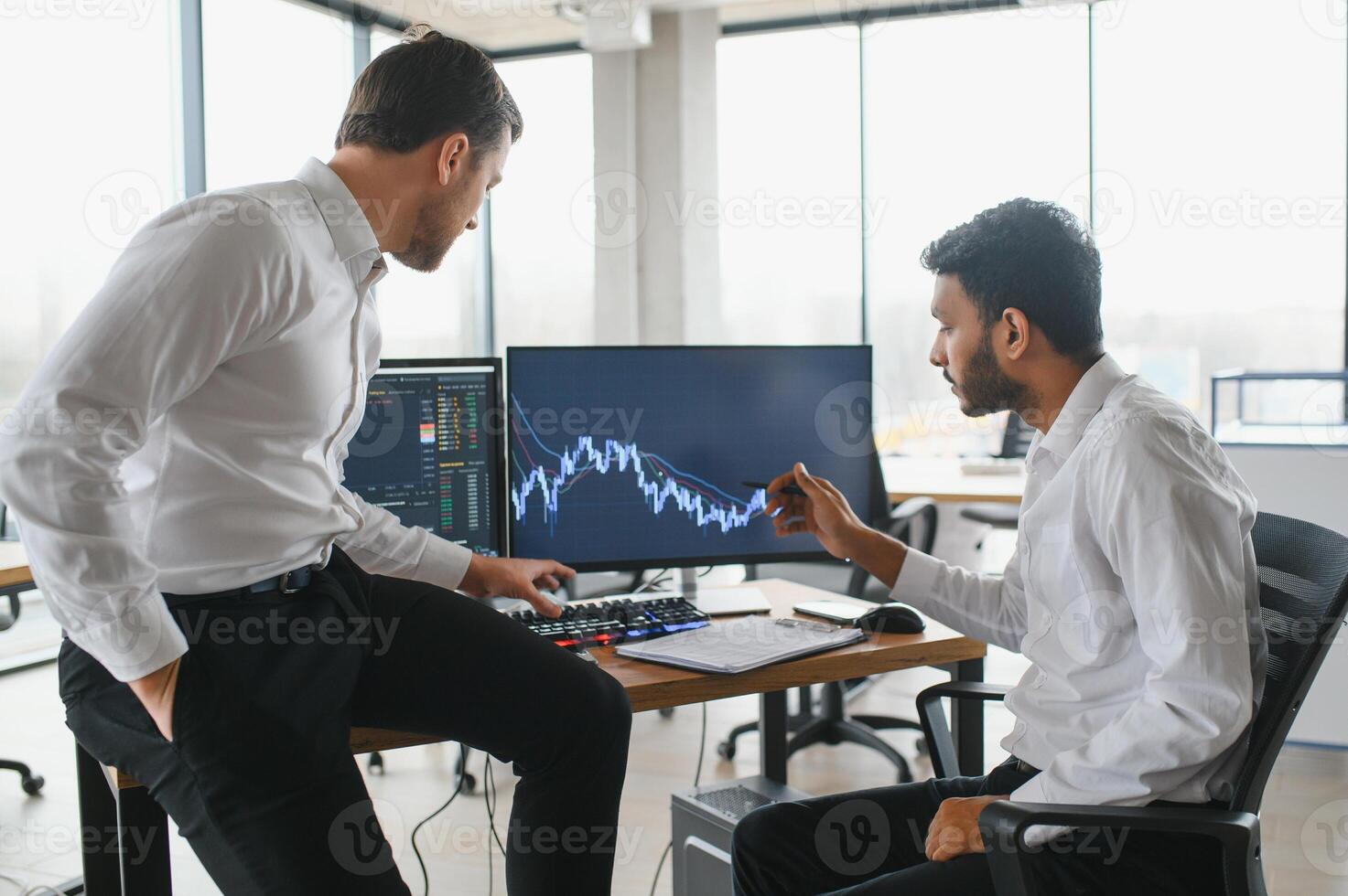 Two men traders sitting at desk at office together monitoring stocks data candle charts on screen analyzing price flow smiling cheerful having profit teamwork concept photo