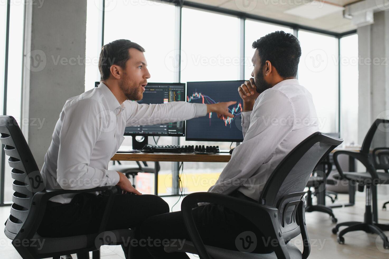 Two men traders sitting at desk at office together monitoring stocks data candle charts on screen analyzing price flow smiling cheerful having profit teamwork concept photo
