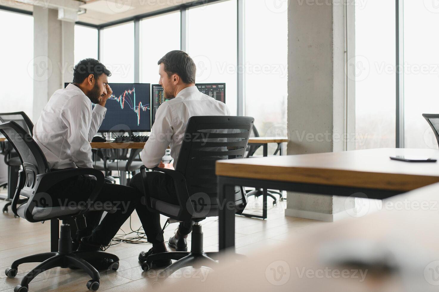 Two men traders sitting at desk at office together monitoring stocks data candle charts on screen analyzing price flow smiling cheerful having profit teamwork concept photo