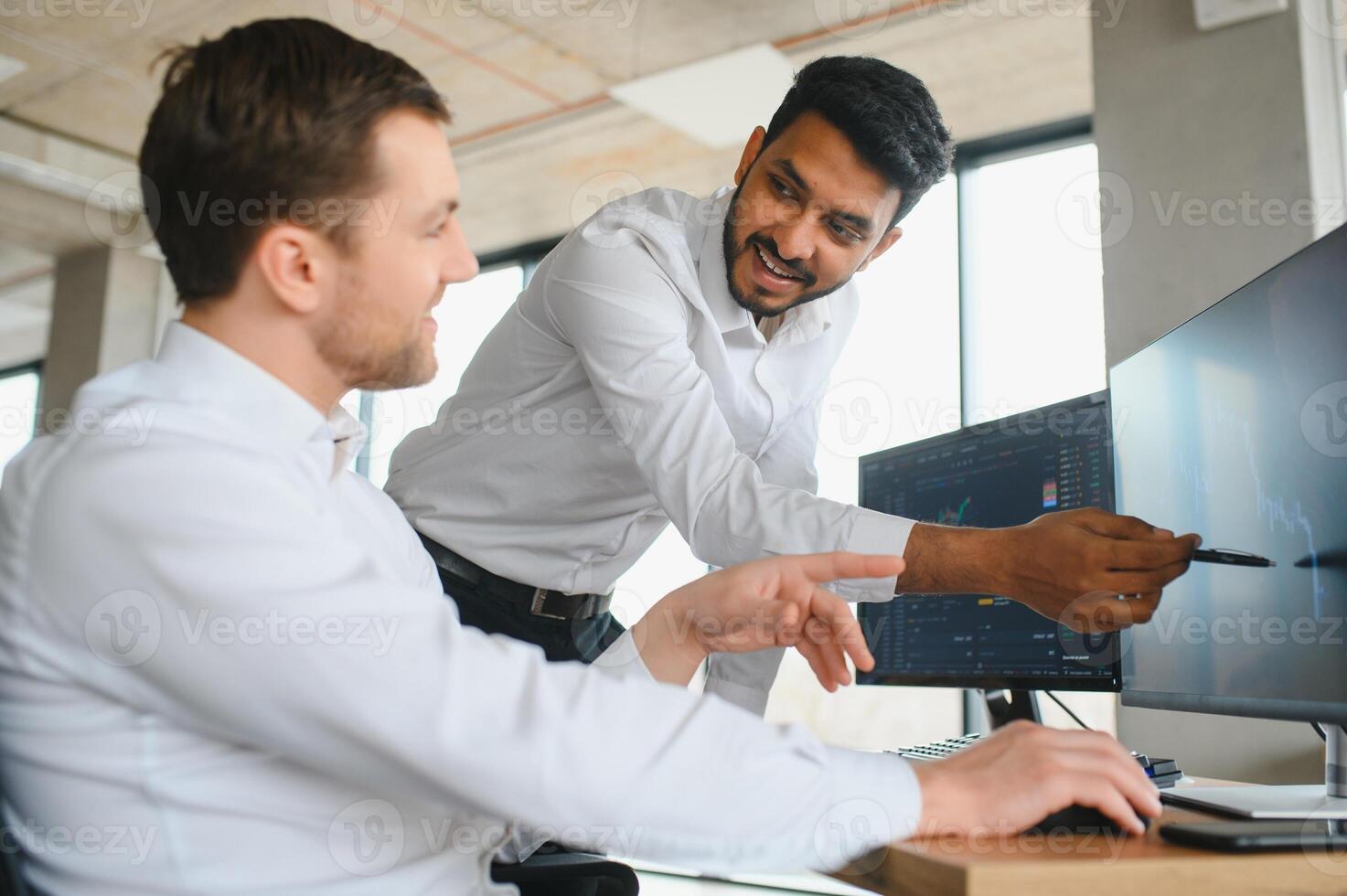 Two successful trader sitting in office and looking at screen, checking cryptocurrency information data on finance market graph, pointing on monitor photo