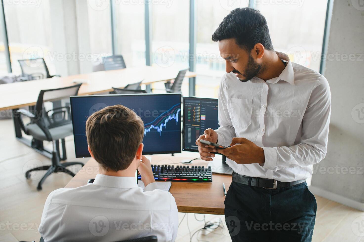 Two successful trader sitting in office and looking at screen, checking cryptocurrency information data on finance market graph, pointing on monitor photo