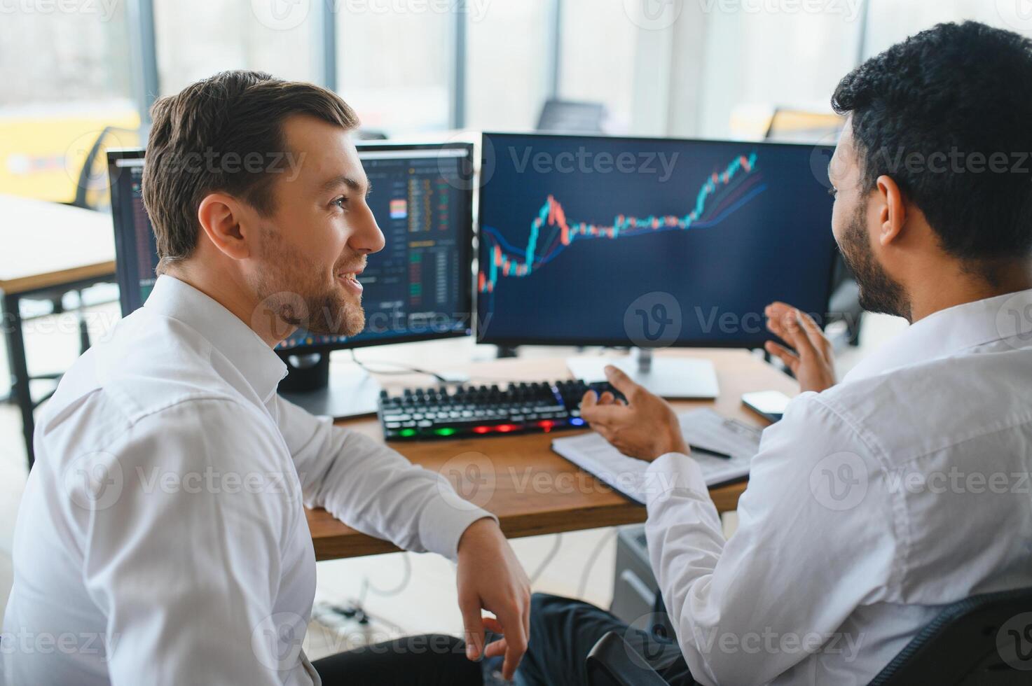 Two successful trader sitting in office and looking at screen, checking cryptocurrency information data on finance market graph, pointing on monitor photo