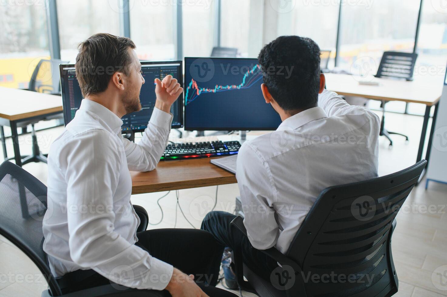 Two successful trader sitting in office and looking at screen, checking cryptocurrency information data on finance market graph, pointing on monitor photo