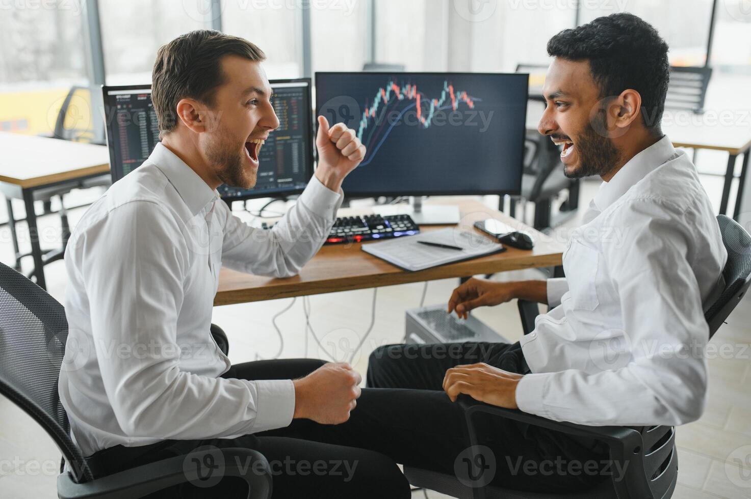 Two men traders sitting at desk at office together monitoring stocks data candle charts on screen analyzing price flow smiling cheerful having profit teamwork concept photo