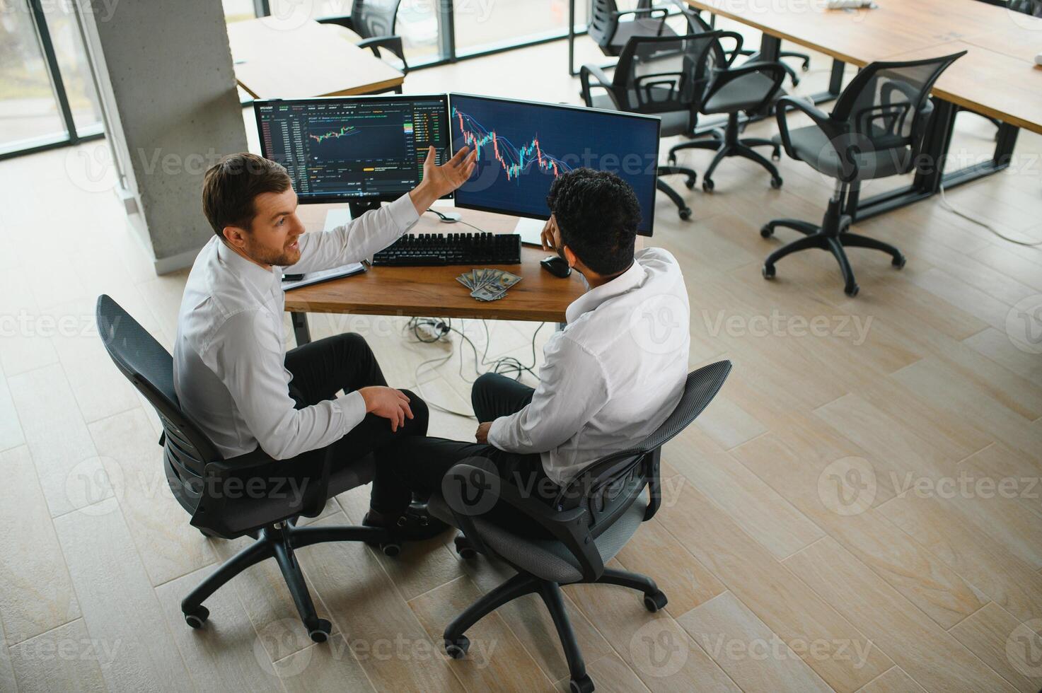 Two men traders sitting at desk at office together monitoring stocks data candle charts on screen analyzing price flow smiling cheerful having profit teamwork concept photo