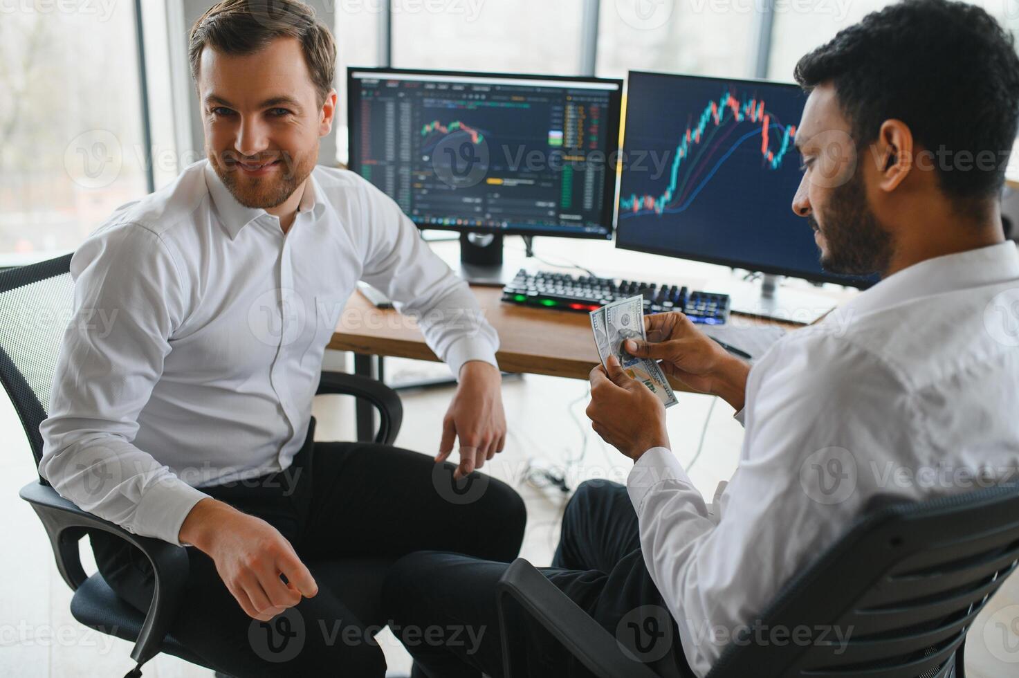 Two men traders sitting at desk at office together monitoring stocks data candle charts on screen analyzing price flow smiling cheerful having profit teamwork concept photo
